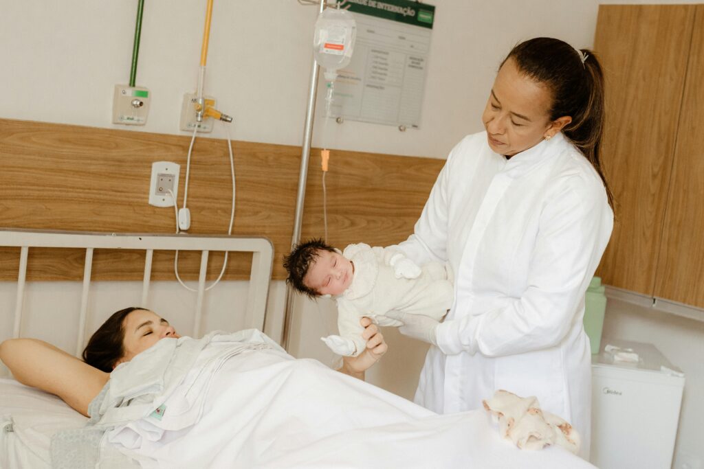 A doctor assists a new mother with her newborn baby in a hospital room setting.